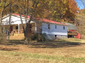 White house with red roof, porch, and attached deck on a hill with fall foliage.